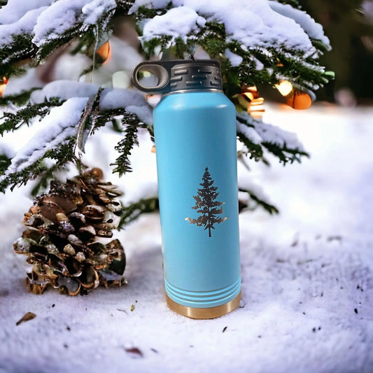 Blue polar camel water bottle with tree design placed in snowy setting.
