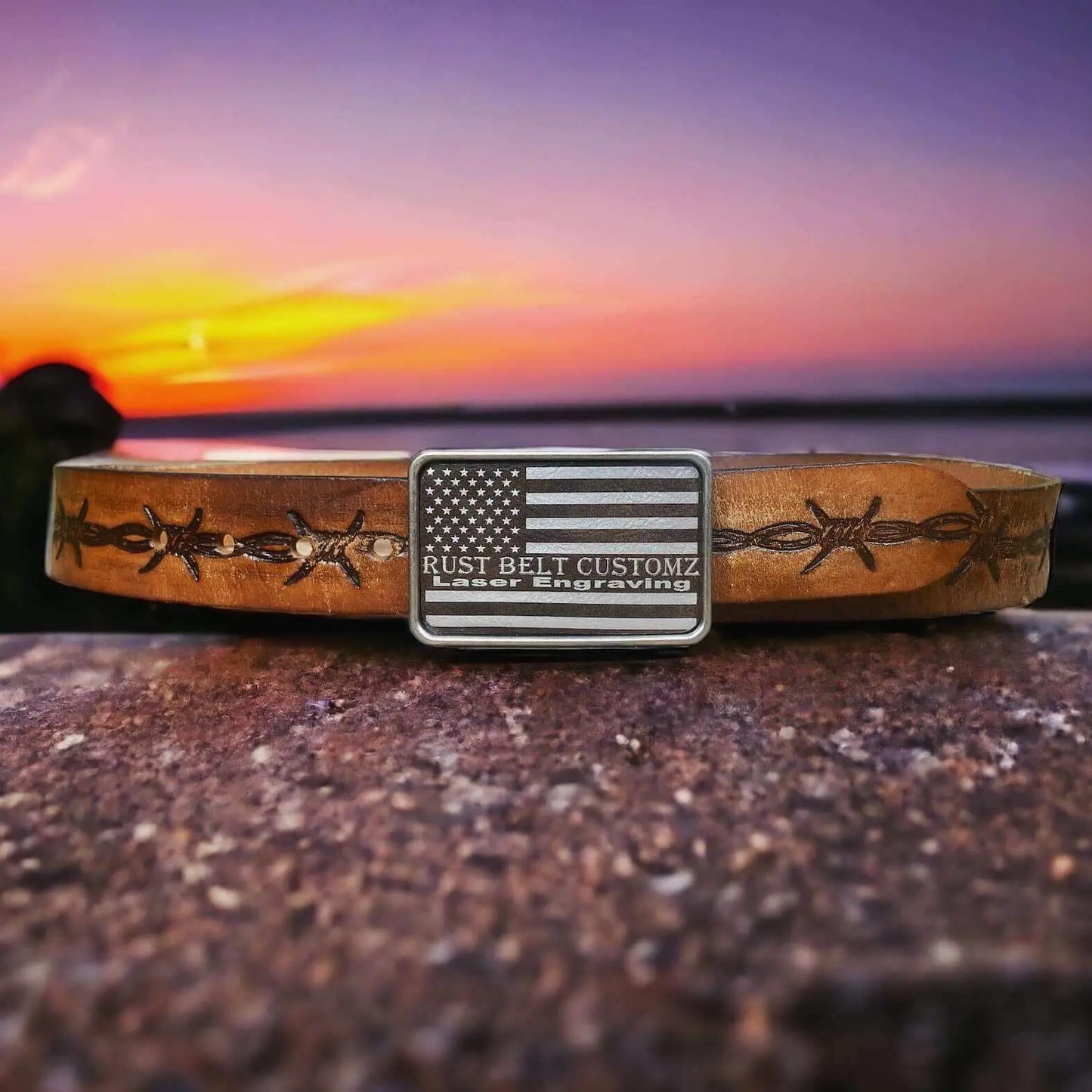 Custom Leather Patch Belt Buckle with American flag design and personalized engraving on a leather belt against a sunset background.