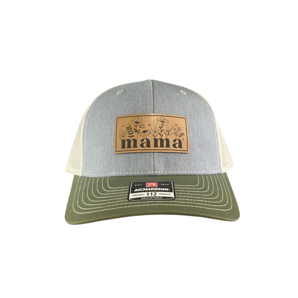 A custom engraved leather patch trucker hat that says "Mama" on the patch with grey on the front, beige mesh on the back half and a green bill, all set on a white background.
