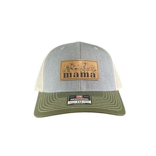 A custom engraved leather patch trucker hat that says "Mama" on the patch with grey on the front, beige mesh on the back half and a green bill, all set on a white background.