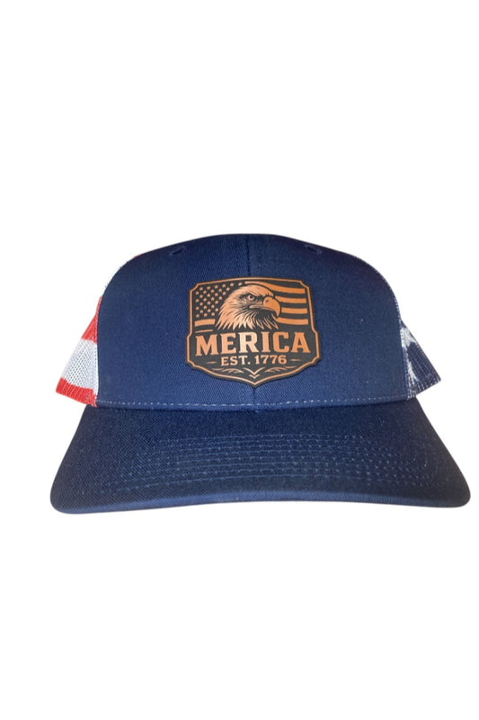 A blue leather patch trucker hat with "Merica" on the patch overtop of an eagle and American flag with American flag mesh on the back half on a white background.