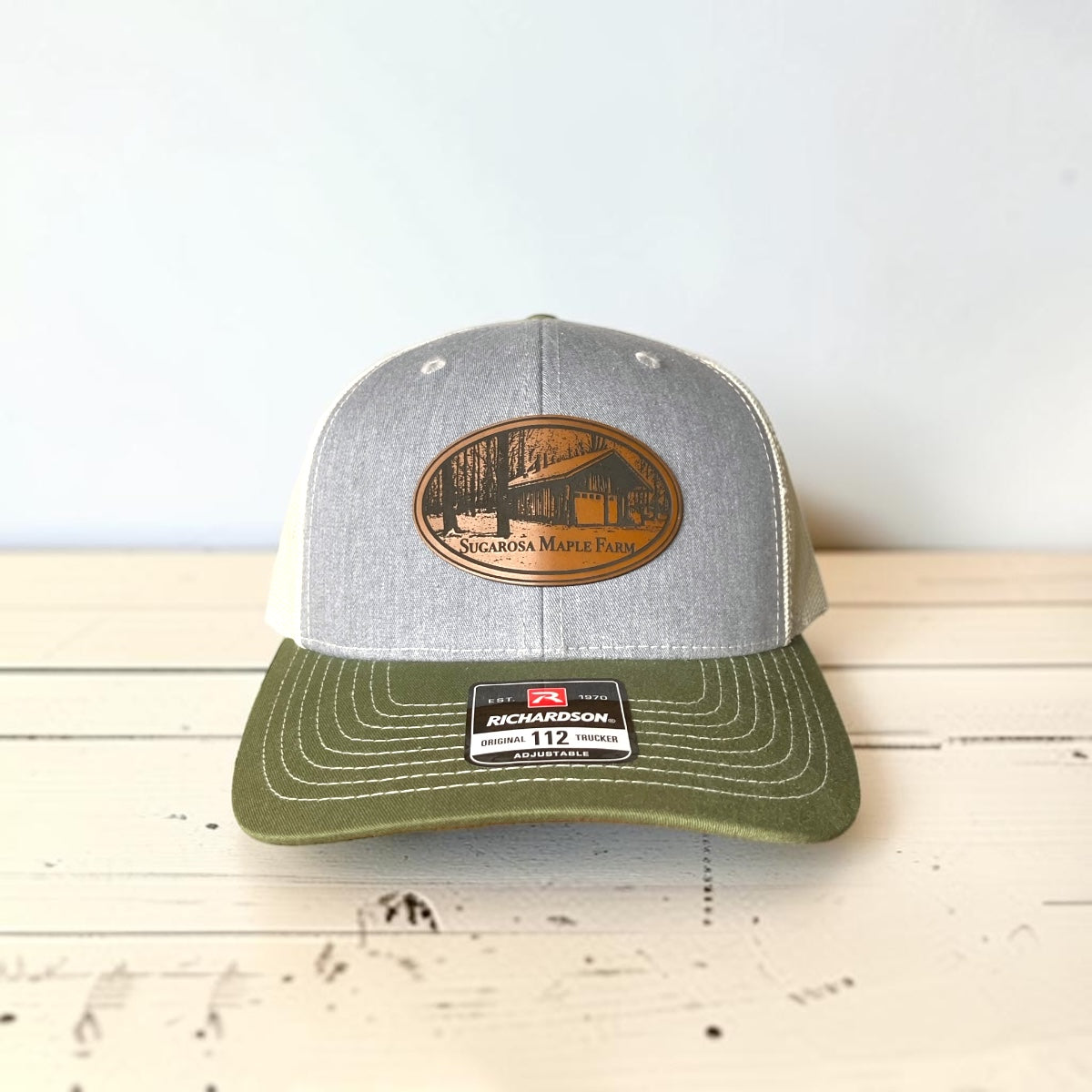 Single black and gray Richardson 112 trucker hat with a tan engraved leatherette sample patch reading Your Logo Here.