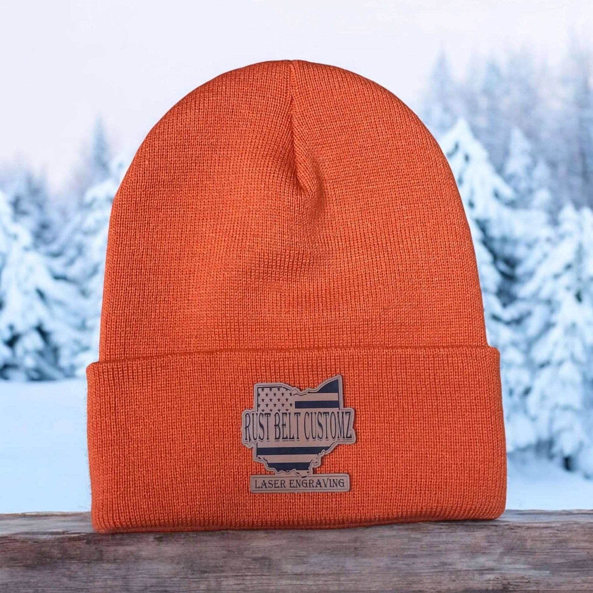 A orange custom engraved leather patch beanie engraved with business background on wooden structure with a winter background.