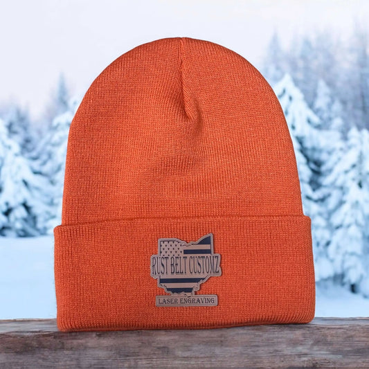 A orange custom engraved leather patch beanie engraved with business background on wooden structure with a winter background.