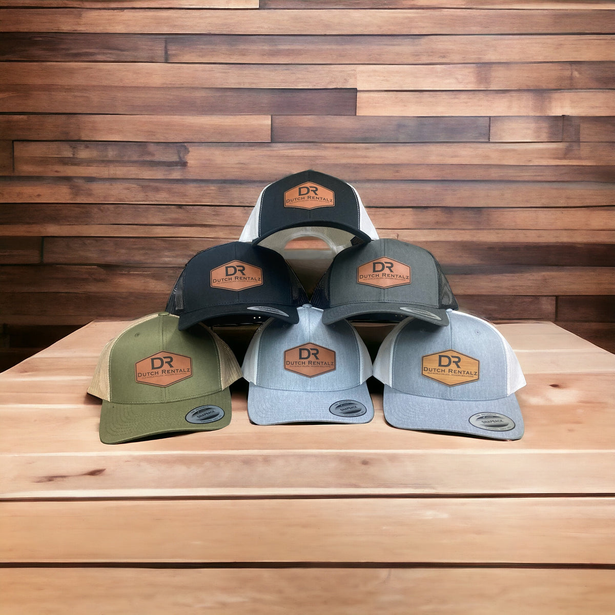 Five finished leatherette patch hats with a custom business logo stacked in front of a wood wall.
