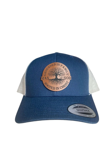 A blue leather patch trucker hat that says "Man of God - Grounded in Family, Rooted in Christ" on the patch with white mesh on the back half of the hat on a white background.